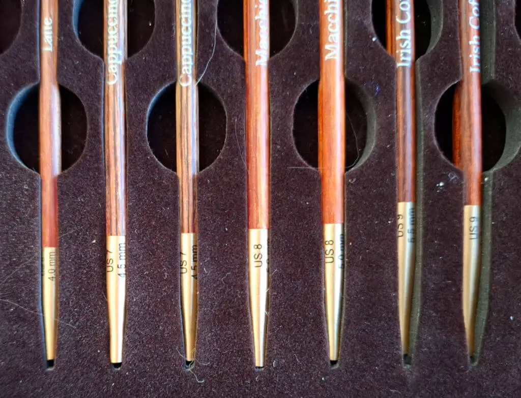 Wooden knitting needles with gold tips, labeled by size, are neatly arranged in a dark, cushioned holder. The needles are marked with names and millimeter sizes | Winwick Mum KnitPro Knit & Sip Set Review