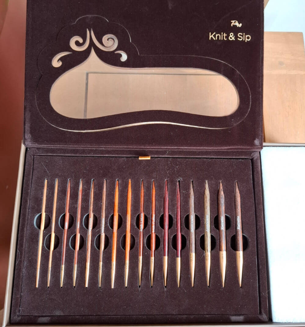 A plush brown box labeled "Knit & Sip" contains various polished knitting needle tips in different sizes, neatly arranged in foam slots, radiating elegance | Winwick Mum KnitPro Knit & Sip Set Review