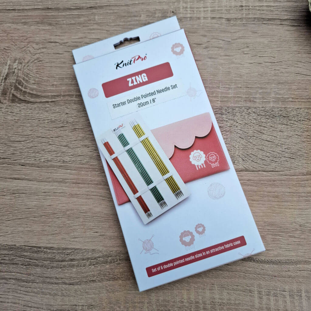 KnitPro Zing double pointed needle set package on a wooden surface. The box displays colourful needles and a pink fabric case with playful icons. KnitPro Zing DPN review