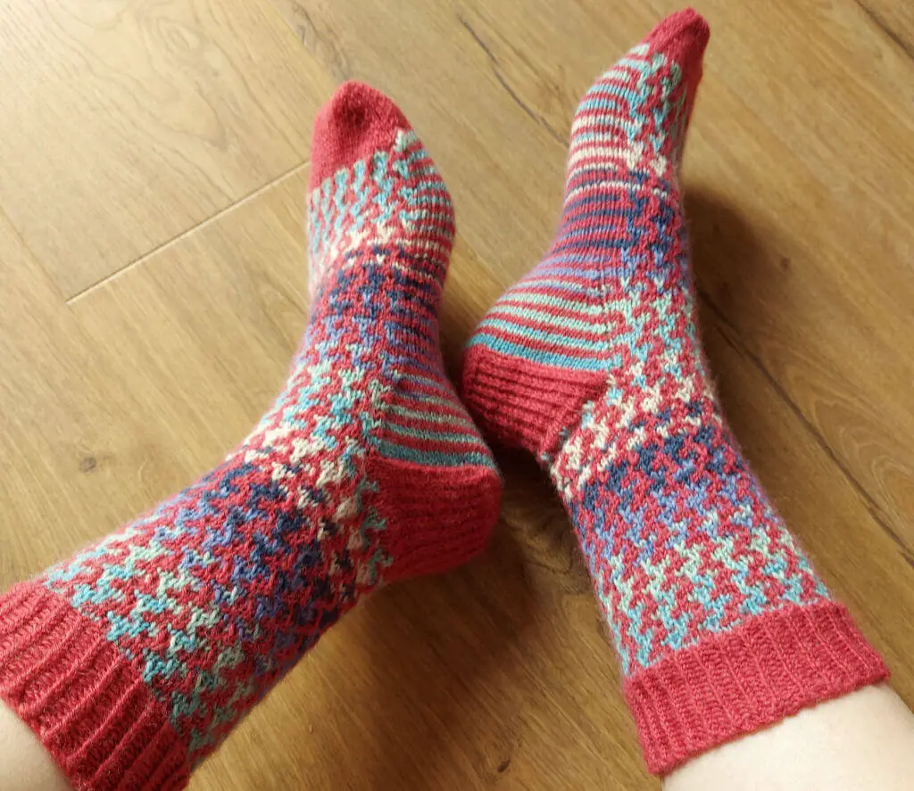 Cozy knitted socks with red, blue, and green patterns on a wooden floor. The playful, colorful design evokes warmth and comfort.