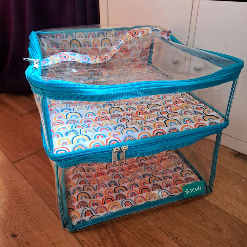 Clear Scubl box storage cube with turquoise trim, featuring a colourful rainbow pattern on the top and bottom surfaces. It's placed on a wooden floor.