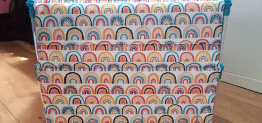 A colourful Scubl storage box with a rainbow pattern sits on a wooden floor, next to an IKEA Kallax unit. The box has a handle and conveys a cheerful vibe. Winwick Mum Scubl box review