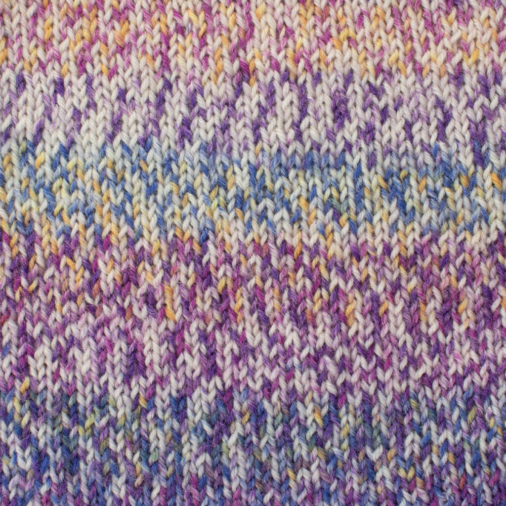 Close-up of colourful West Yorkshire Spinners, Signature 4ply, Purple Emperor knitted fabric featuring a mix of purple, blue, and yellow hues. The texture is soft and warm, conveying a cozy feel.