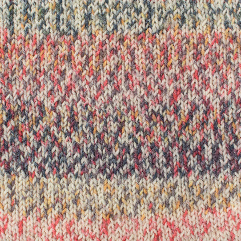 Close-up of West Yorkshire Spinners Signature 4ply, Red Admiral knitted fabric with a colorful mix of pink, yellow, blue, and cream yarns. The texture appears soft and cozy, conveying warmth.