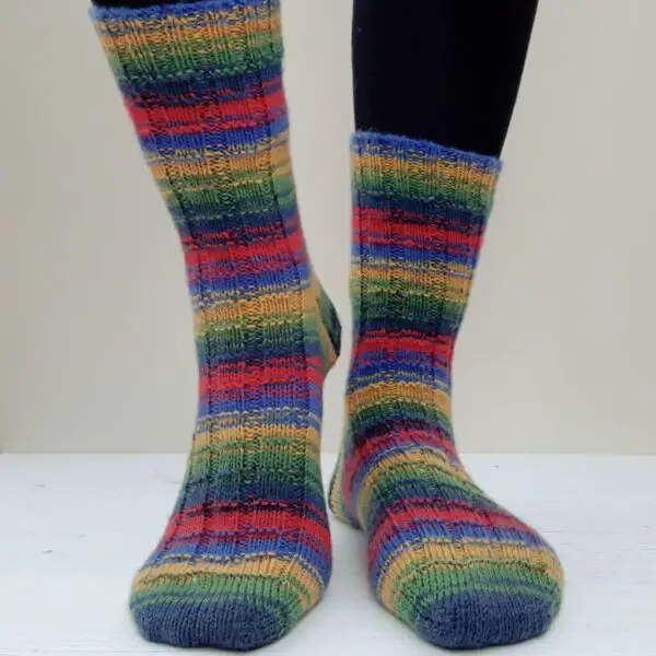Brightly coloured, striped knit socks in shades of red, blue, green, and yellow, worn by a person with black leggings. The mood is cheerful.