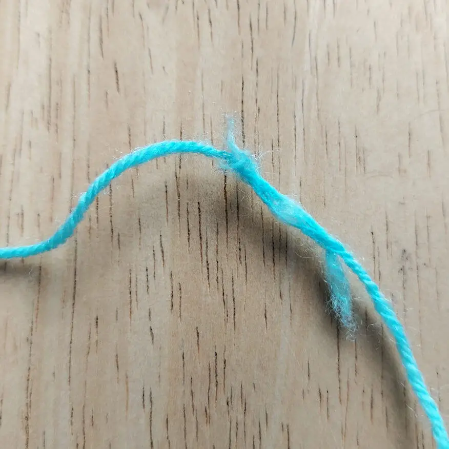 A close-up of a light blue yarn strand on a wooden surface. The yarn is slightly frayed, contrasting against the wood's smooth, light brown texture. Winwick Mum | Free sock knitting patterns | Joins, knots or faults in yarn