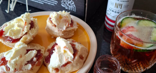 Four half scones with cream and jam on a yellow plate next to a cut glass containing Pimm's and fruit. The empty Pimm's can is next to the glass.