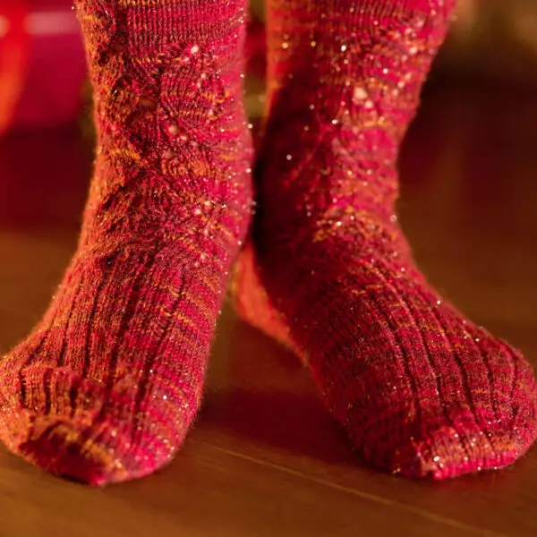 Close-up of cozy, glittery red socks on a wooden floor, with a soft warm glow. The knit texture adds a festive touch to the scene.