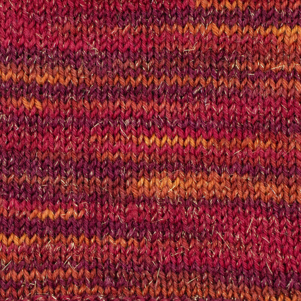 A colourful knitted fabric with interwoven shades of red, orange, and purple, creating a warm, cosy texture. The pattern is textured with some shiny threads.