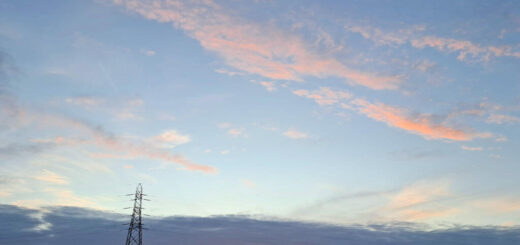 Sunset over a countryside landscape with a silhouetted pylon. The sky features soft pink and blue hues, creating a serene atmosphere.