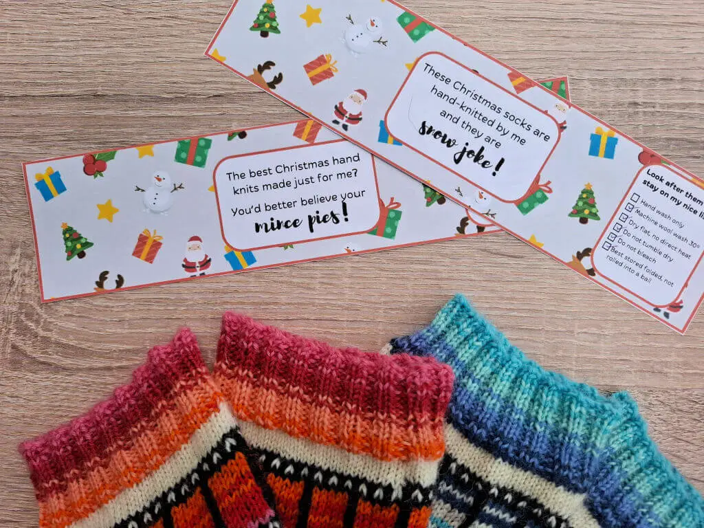 Knitted socks in vibrant stripes are paired with playful Christmas-themed labels featuring snowmen and gifts, creating a festive and cozy mood.