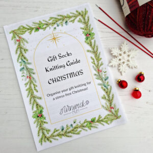 Winwick Mum gift knitting guide cover with Christmas theme, bordered by pine branches and holly. Festive decor includes baubles, a snowflake, a ball of yarn and knitting needles.