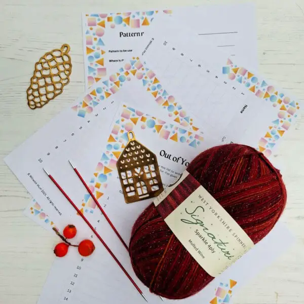Red yarn, gold knitting tools, and red needles on colourful printed sheets. Bright, inviting crafting scene with a holiday, cosy feel.