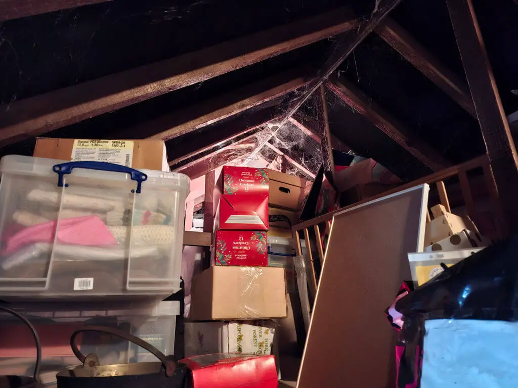 Attic filled with stacked boxes and storage containers, draped in cobwebs. Dim lighting and shadows create a nostalgic, cluttered atmosphere.
