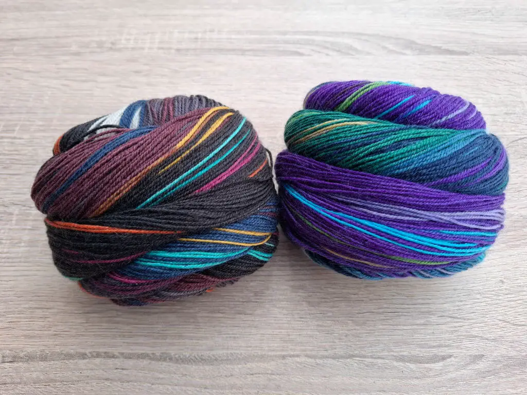 Two balls of multicoloured yarn on a wooden surface. The left ball has dark and warm tones, while the right has cool colours, emphasising contrast.
