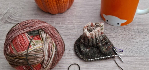 A cosy scene with a ball of multicoloured yarn partially knitted, a pumpkin-shaped container, and a mug of tea on a wooden table. Warm autumn vibes.