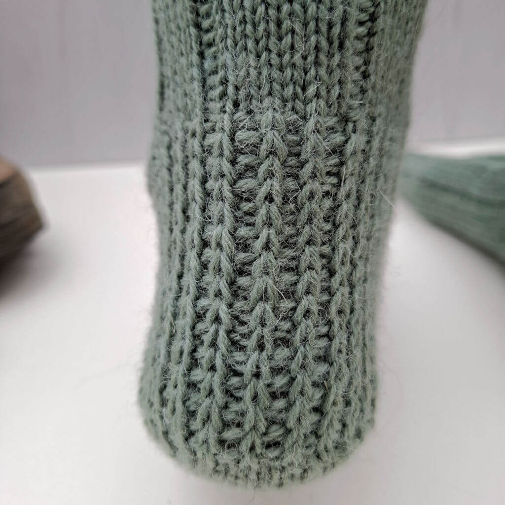 Close-up of a textured green knit fabric showcasing intricate vertical ribbing patterns. Warm and cozsy vibe, with subtle lighting enhancing the texture.