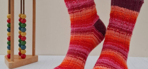 Person wearing vibrant, striped socks in red, orange, and pink hues stands on a light wooden floor. An abacus with colourful beads is next to them.
