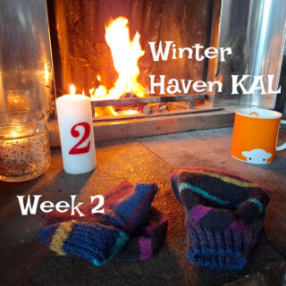 Cosy scene by a lit fireplace with striped knit socks, a red-numbered candle, and an orange mug. Text reads, "Winter Haven KAL, Week 2."
