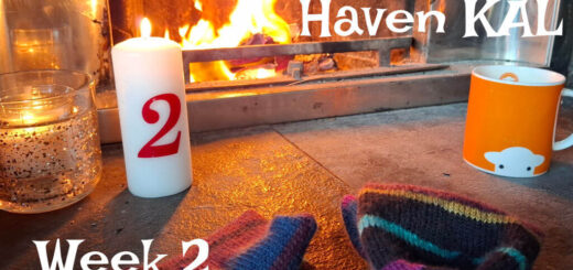 Cosy scene by a lit fireplace with striped knit socks, a red-numbered candle, and an orange mug. Text reads, "Winter Haven KAL, Week 2."