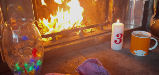 Cosy fireplace scene with yarn, a colourful vase, a lit candle marked “3,” and an orange mug. Text reads “Winter Haven KAL Week 3,” conveying warmth.