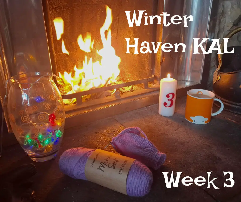 Cosy fireplace scene with yarn, a colourful vase, a lit candle marked “3,” and an orange mug. Text reads “Winter Haven KAL Week 3,” conveying warmth.