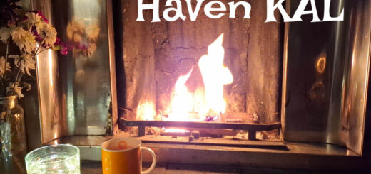 Cosy fireplace with flames glowing warmly. Flowers in a jar, a lit candle, and an orange mug are on the hearth. Text reads “Winter Haven KAL, 9-30 January 2026.”