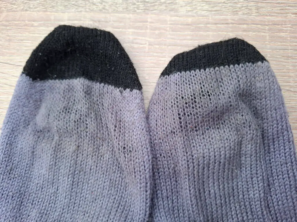 Close-up of a pair of purple socks with black toes, lying on a wooden surface. The socks appear worn with visible thinning.