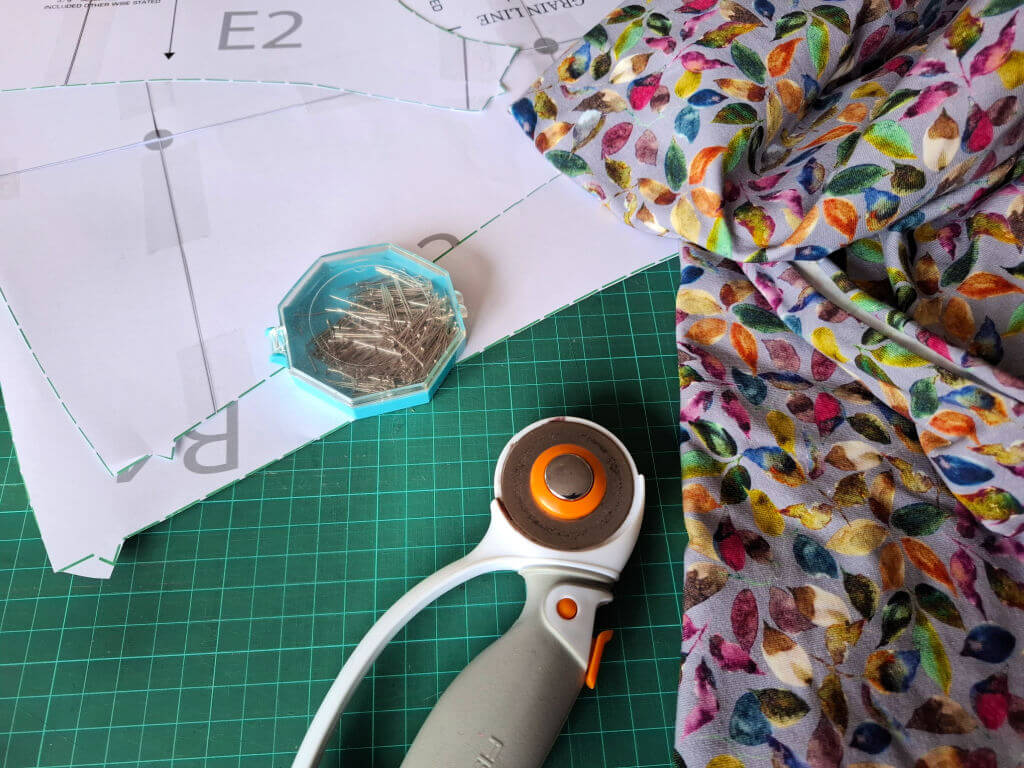 Sewing setup with colourful fabric, pattern paper, rotary cutter, and pins on a green cutting mat. The bright colours convey creativity.