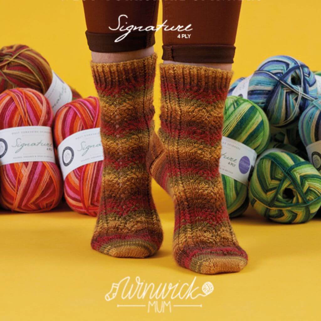 Knitted socks in autumn hues are displayed against a bright yellow backdrop, surrounded by vibrant balls of yarn in various colours.