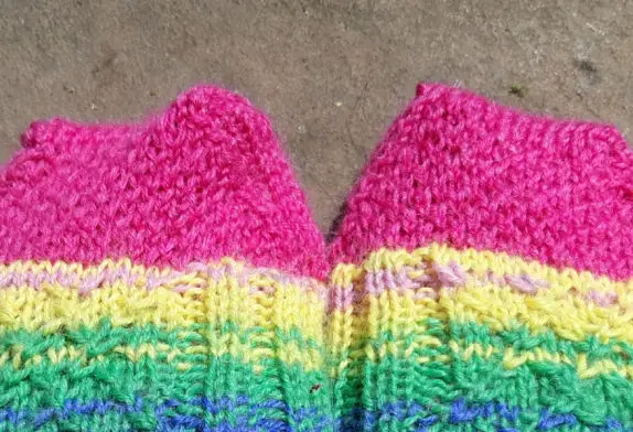 Brightly coloured knitted socks with pink toes and a pattern of yellow, green, and blue stripes. The texture is warm and cosy on a neutral background.