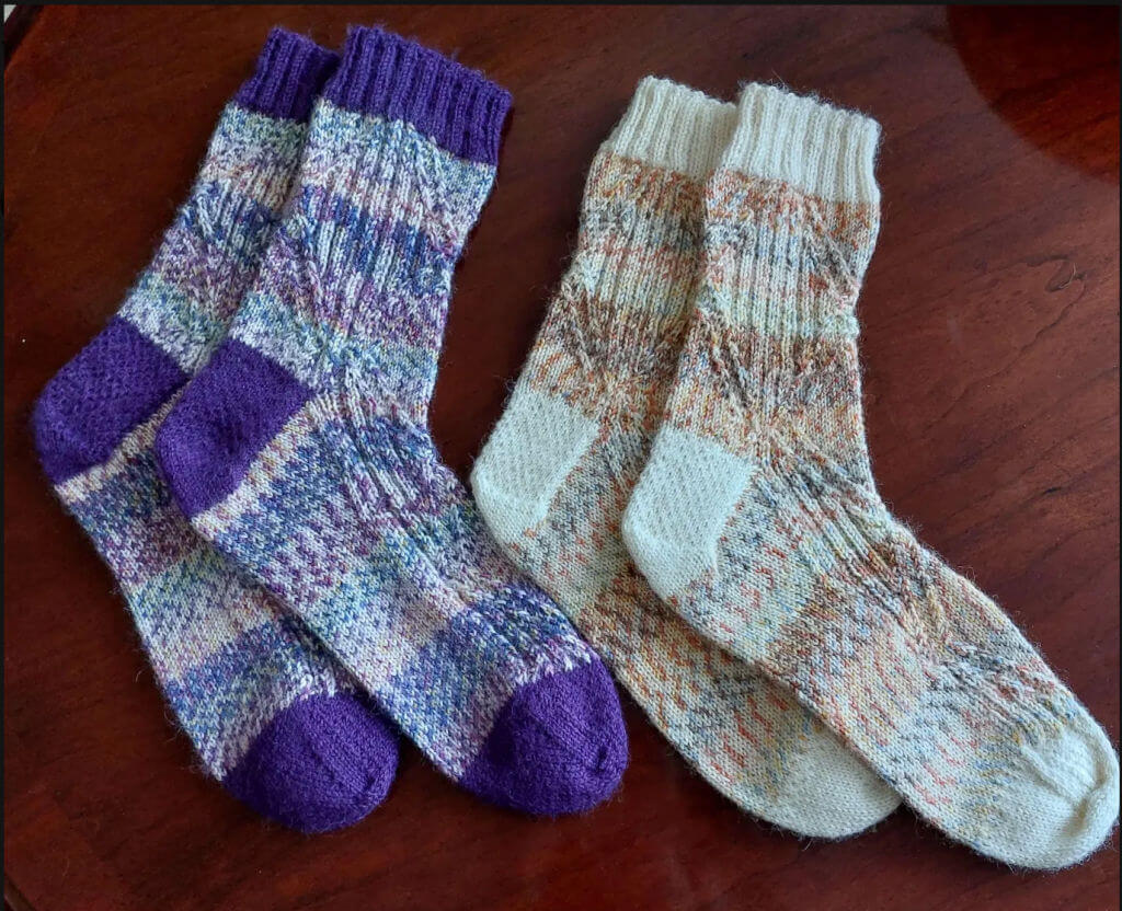 Two pairs of knitted socks on a wooden surface. The left pair is purple and multicoloured, while the right is in earthy tones with beige accents.