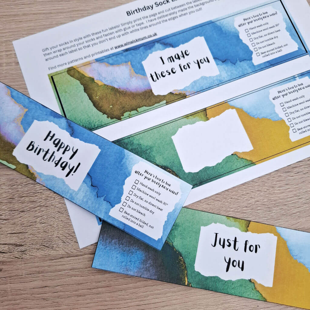 Colourful sock labels with textured watercolour backgrounds on a wooden surface. Messages include "Happy Birthday!" and "I made these for you" in playful fonts.