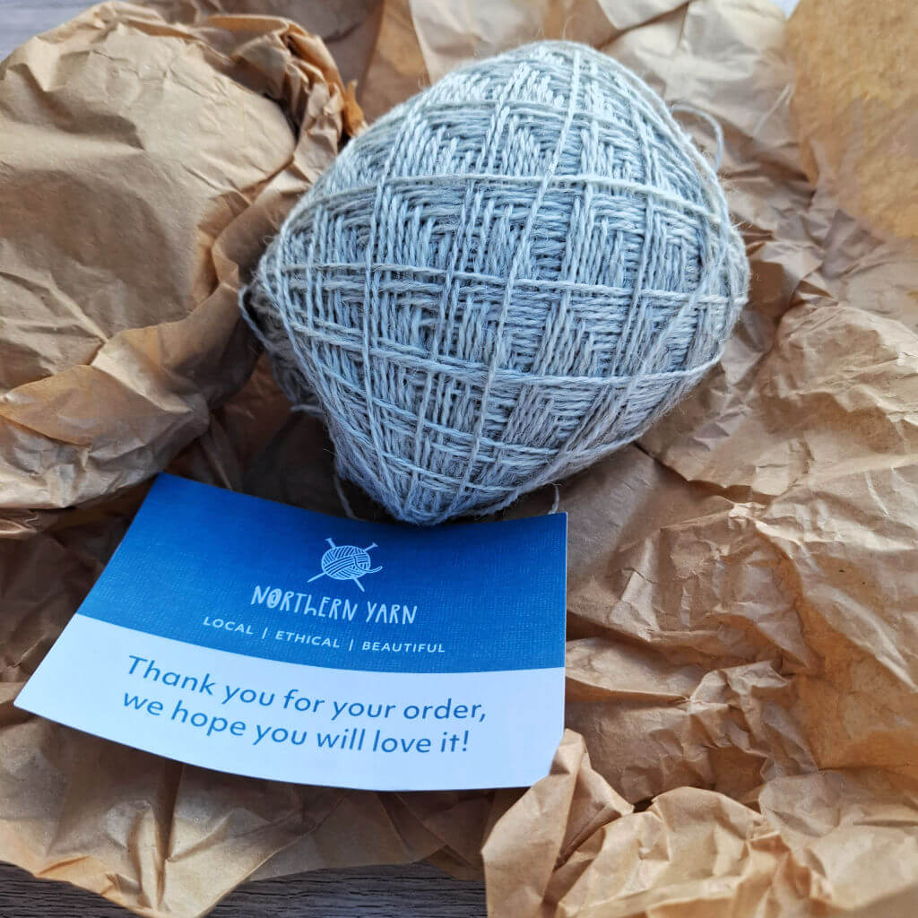 A ball of grey yarn rests on crumpled brown paper, accompanied by a blue card from "Northern Yarn" expressing gratitude for the order.