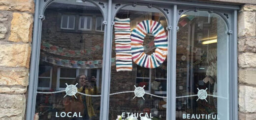 Shop window with "Local, Ethical, Beautiful" decals. Display features a colourful yarn "10" and white flowers, conveying a welcoming, creative vibe.