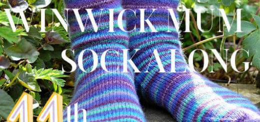 Two feet wearing colourful striped knitted socks in a garden setting with green foliage. Text overlay reads "Winwick Mum Sockalong 11th Birthday."