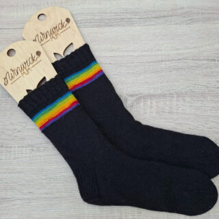 Black socks with vibrant rainbow stripes near the top, displayed with wooden sock blockers. The scene conveys warmth and comfort.