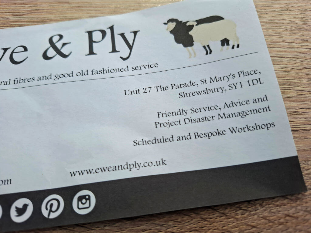 Alt text: Close-up of a brochure on a wooden surface for "Ewe & Ply," featuring text about services and contact details, with a sheep logo.