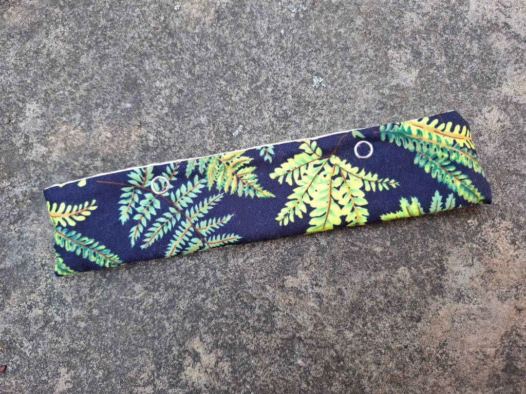 A fabric pouch with a vibrant fern pattern in green and yellow against a dark blue background. It lies on a textured stone surface.