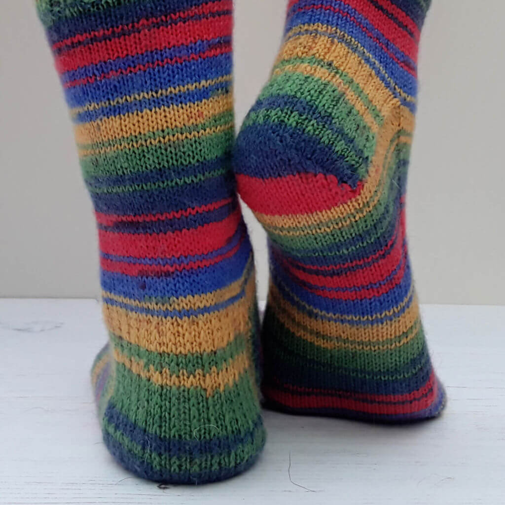 A close up of the heel flap of a pair of socks knitted in brightly coloured self-striping yarn